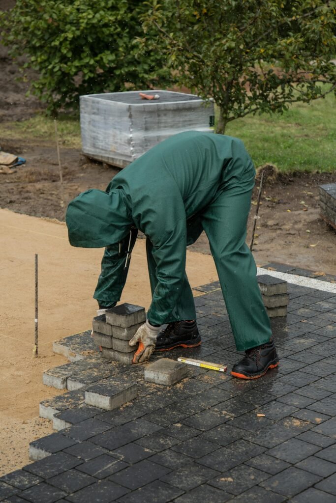 Man laying pavers in an outdoor setting, wearing green rain gear. Concept of construction work.